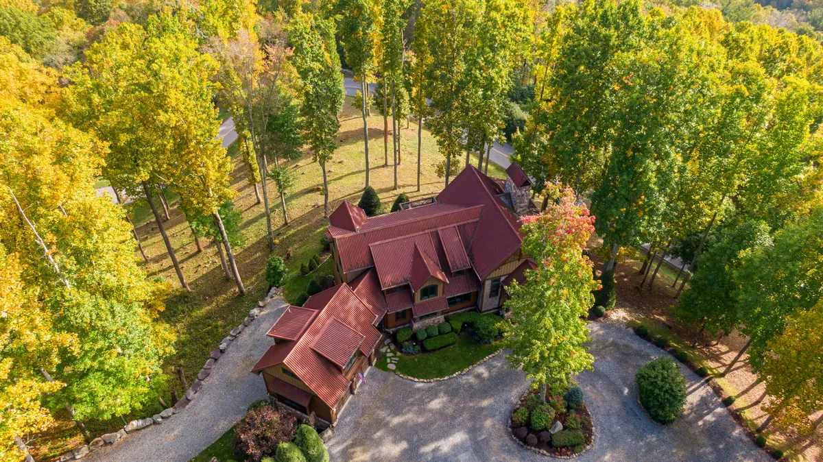 An exterior view of the house with a striking red roof, nestled among tall trees and featuring a circular driveway. The image conveys a sense of seclusion, natural beauty, and ample outdoor gathering spaces.