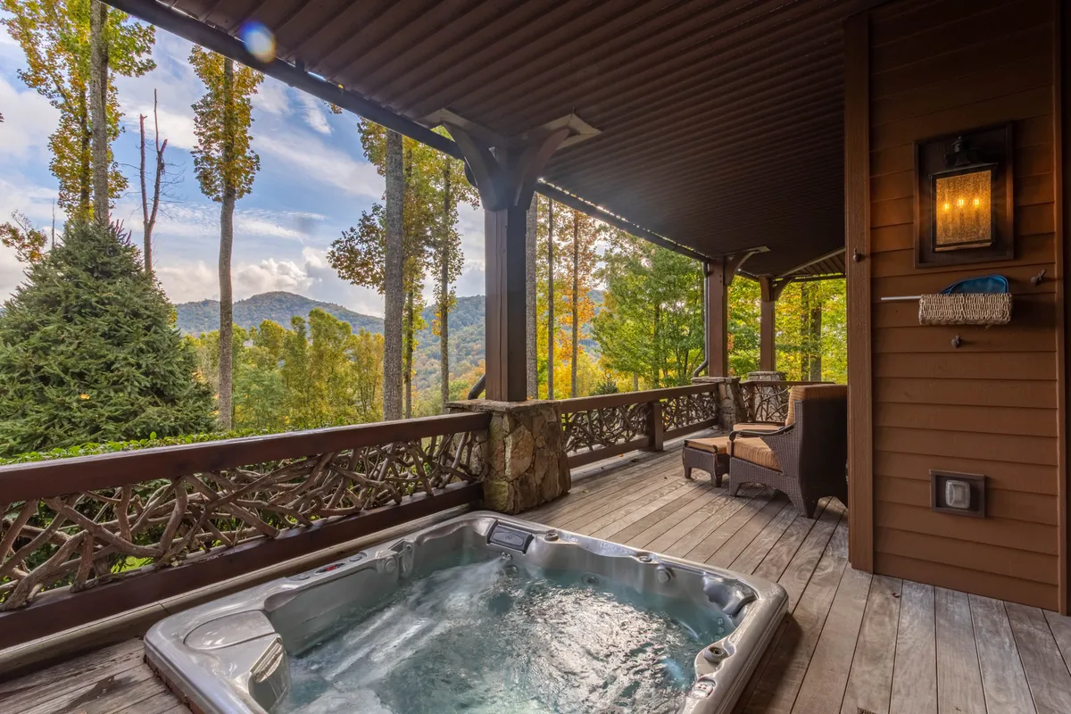 An exterior shot of the lower deck with a bubbling jacuzzi/hot tub, wooden railings, mountain views, and comfortable seating. The setting is tranquil, with hints of nature all around, inviting guests to unwind after a day of adventure.
