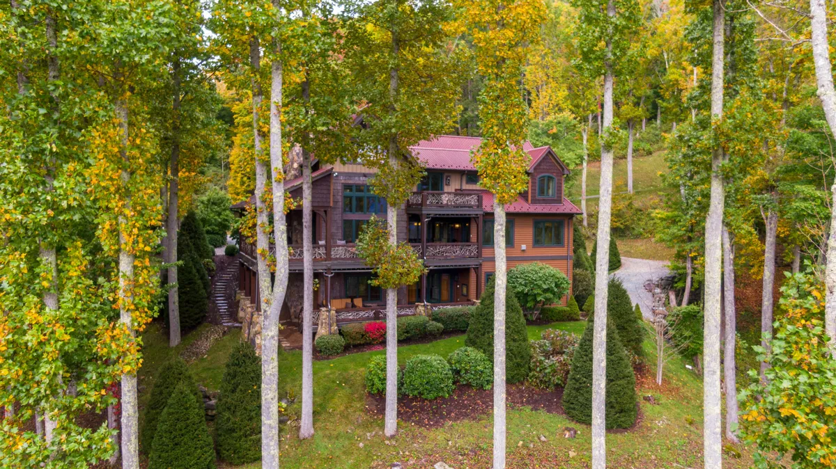 The exterior of the house is set amidst tall trees and manicured shrubs, with a gentle pathway leading toward the home. The setting suggests tranquility, privacy, and immersion in nature—ideal for romantic getaways or small group escapes.