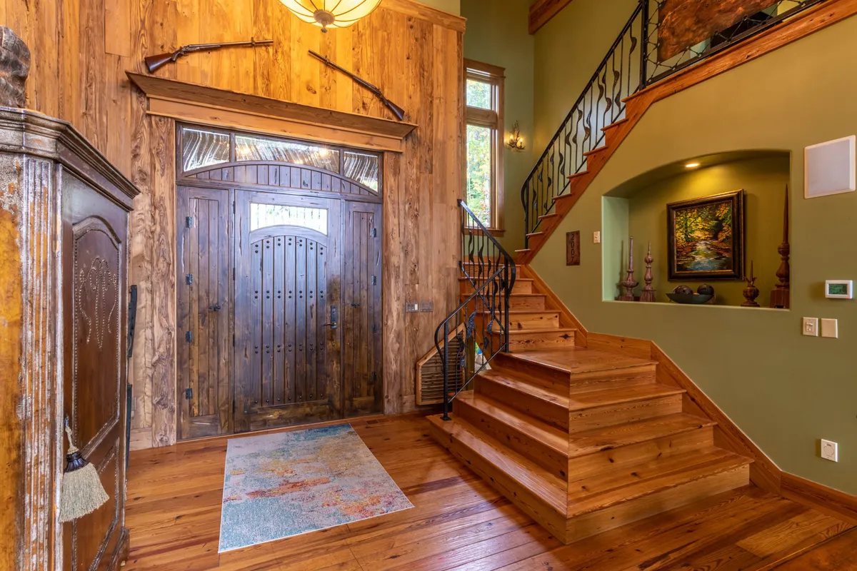 The image captures the home's large wooden front door, a spiral staircase, and inviting decorative artwork in the entryway. Natural light filters through, hinting at the transition from outside to in, and evoking a sense of arrival and anticipation for what's beyond.