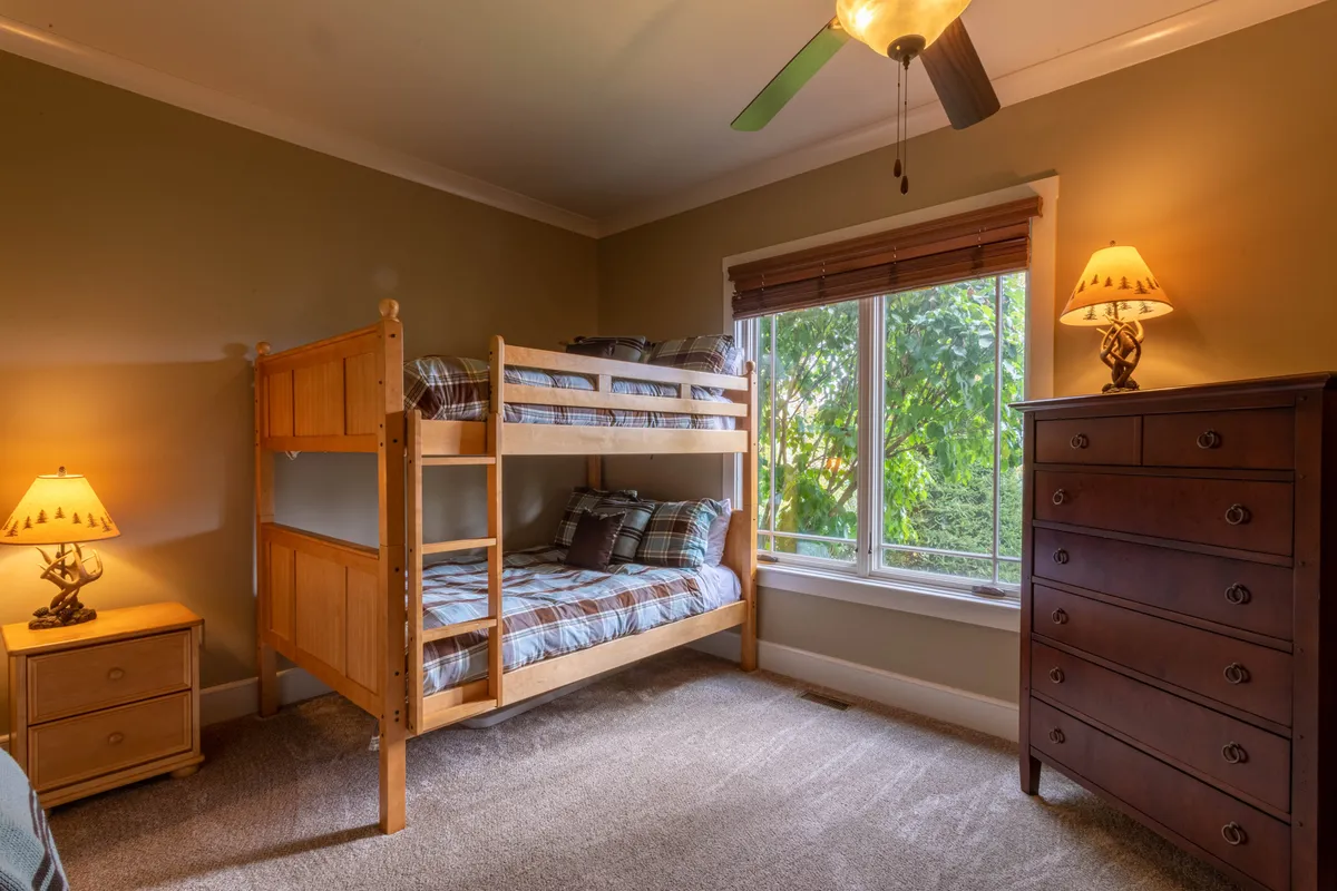 A playful and inviting bunk room features queen-over-queen bunk beds, a dressing table, and cheerful decor. Natural light streams in from the window, and lamps provide a warm glow for late-night chats or reading. The room is designed with both comfort and whimsy, perfect for children or groups.