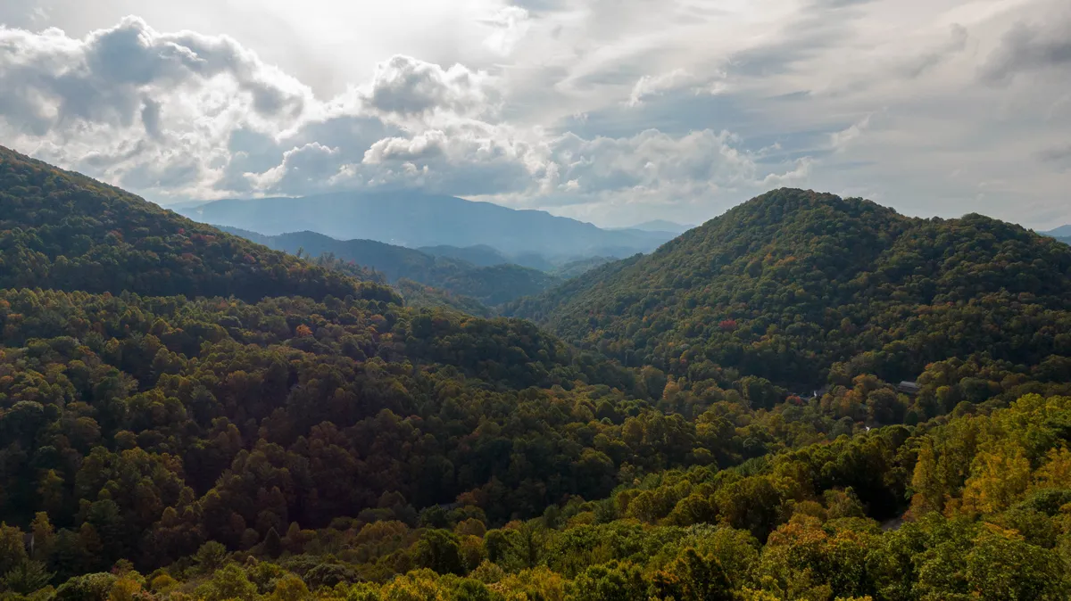 A panoramic view of rolling hills, dense forests, and distant mountains beneath a wide sky. The vantage point evokes the feeling of being high above, with untouched wilderness stretching to the horizon—ideal for hiking, scenic strolls, or simply soaking in nature’s grandeur.