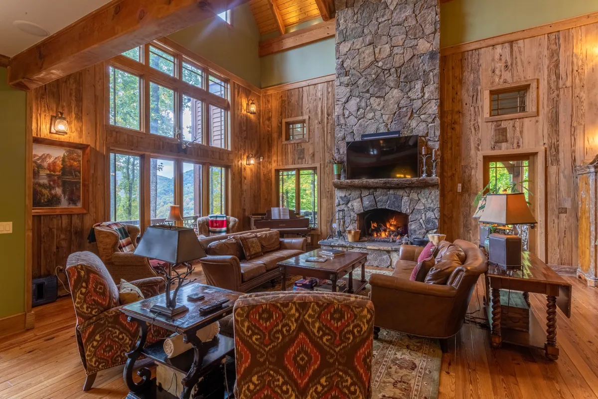 A spacious living area with a large stone fireplace, comfortable seating, expansive windows brimming with natural light, and decorative artwork. The setting conveys warmth, leisure, and the perfect place to relax after outdoor activities.