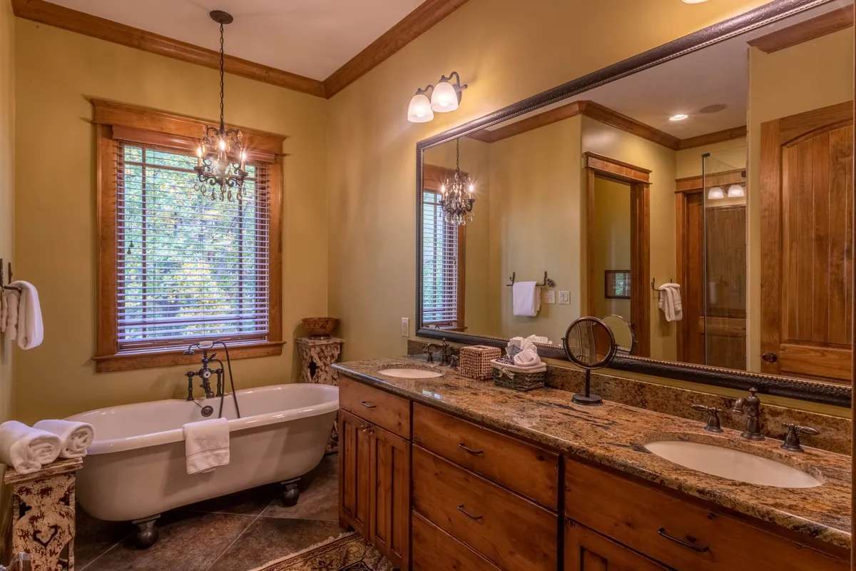 A spa-like bathroom with a freestanding bathtub, double vanity with sinks, a large mirror, and elegant chandelier lighting. The space exudes tranquility and luxury, designed for relaxation and self-care.