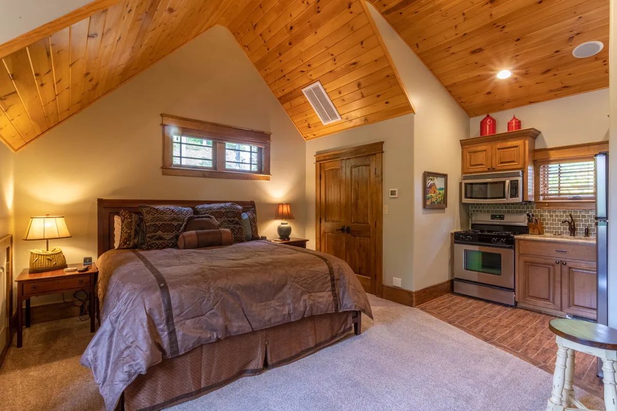 This image depicts a comfortable suite with a plush bed adorned with decorative pillows, a nightstand with a lamp, and a convenient kitchenette area. The space feels both homey and independent, ideal for guests seeking privacy and the ability to prepare their own meals.