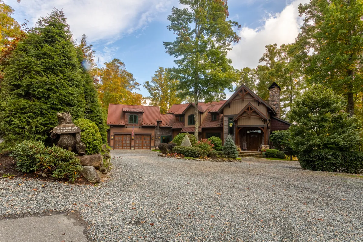 The home’s main entrance is framed by a stone chimney, manicured gardens, and a welcoming driveway. The landscaped setting hints at outdoor entertaining spaces, while the architecture blends mountain lodge elegance with a sense of privacy and comfort.
