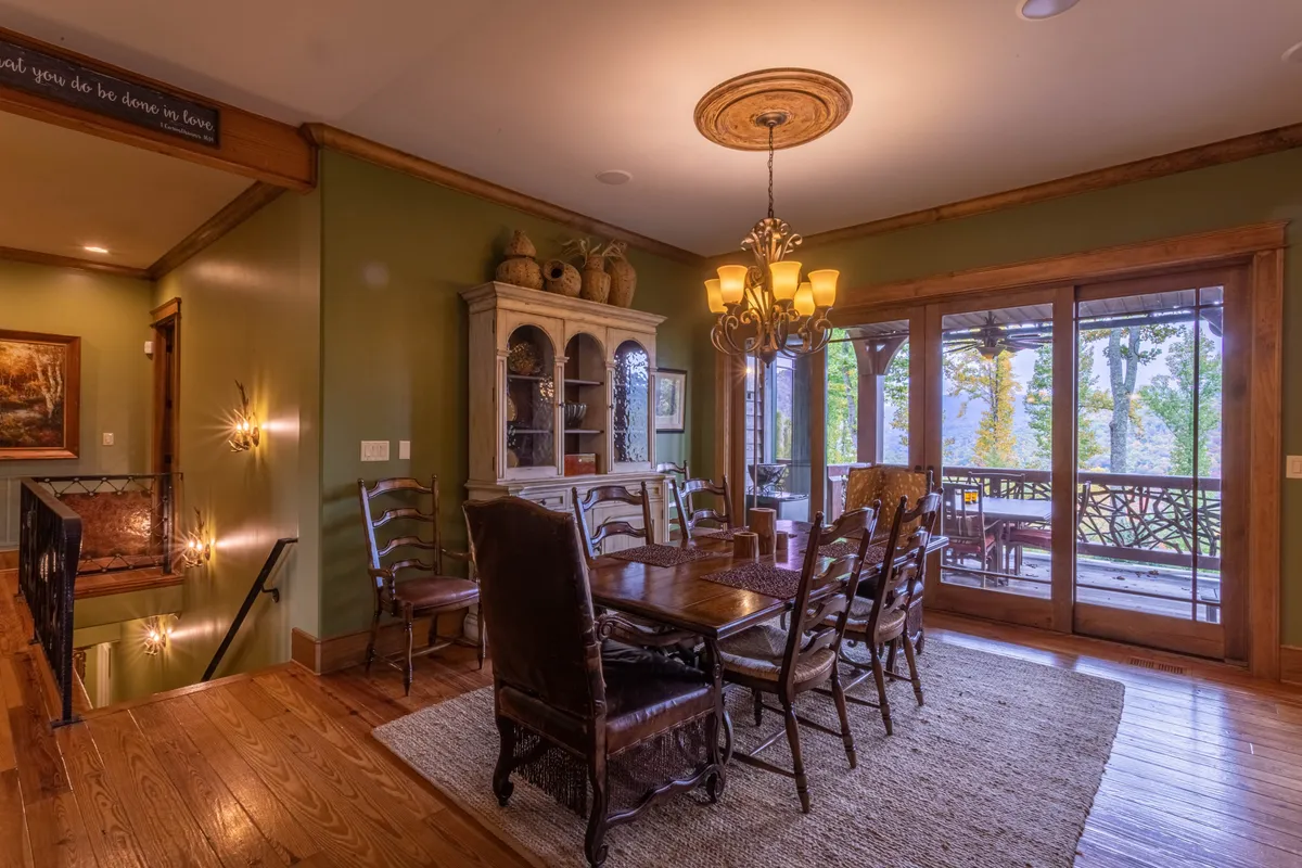 An elegant dining area with a spacious table set for ten, positioned beneath a striking chandelier. The space is surrounded by warm wood tones, designer lighting, and large windows that frame scenic outdoor views, creating an atmosphere of celebration and togetherness.