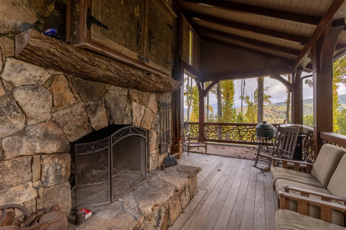 A cozy living space featuring a stone fireplace, wooden furniture, and expansive windows with views overlooking the surrounding landscape. The ambiance is both inviting and connected to nature, showcasing the interplay of comfort and the great outdoors.