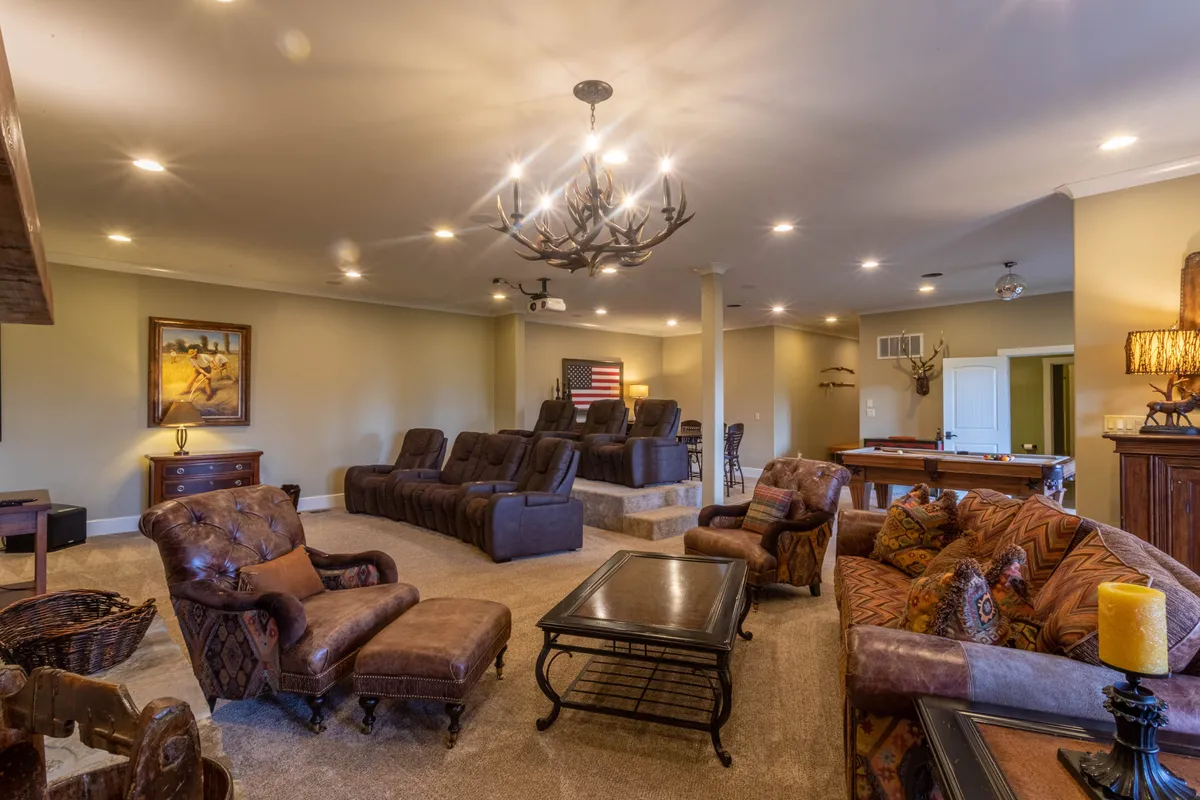 This image showcases a spacious entertainment area featuring cinema-style seating, a pool table, a sparkling chandelier, and vibrant artwork. The arrangement suggests an inviting atmosphere for both gaming and movie nights, with ample space for socializing and relaxation.