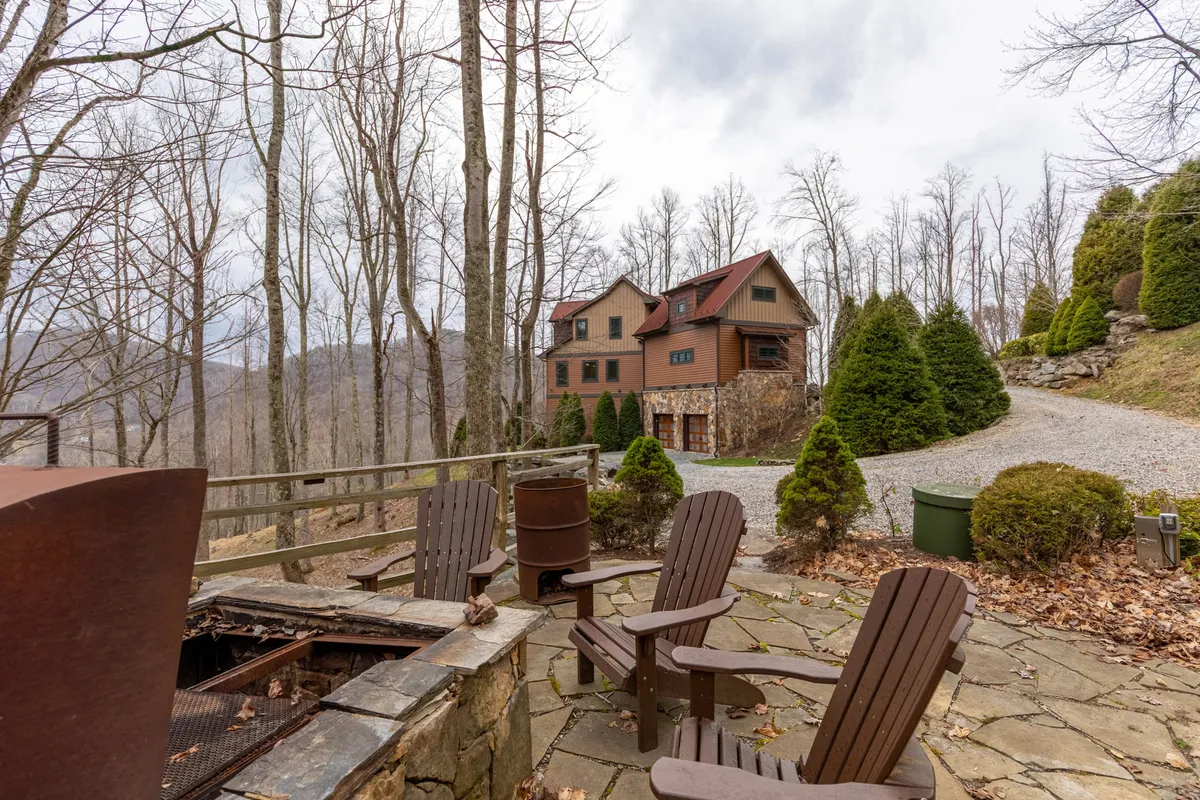 A calm, inviting stone patio set with wooden chairs, nestled amongst tall trees with the house in the background. The setting is perfect for relaxing by the fire pit, gathering with friends or family, and embracing the peaceful mountain air. The outdoor space feels both communal and private, ideal for evening gatherings or unwinding after a day of activity.